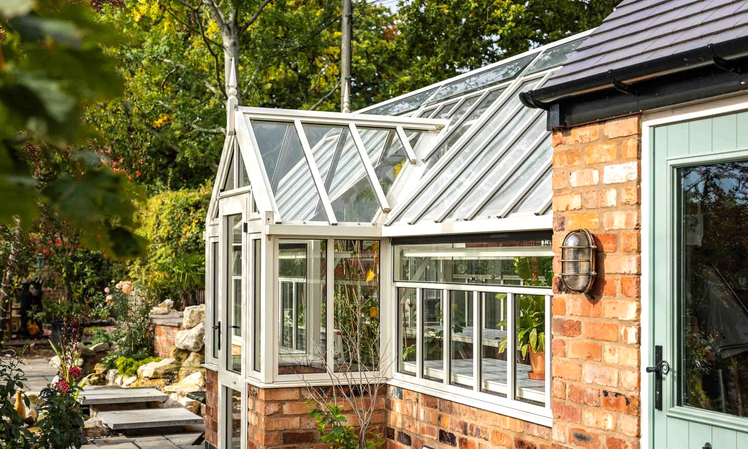 Cultivar Victorian glasshouse installed against a brick house in a mature garden