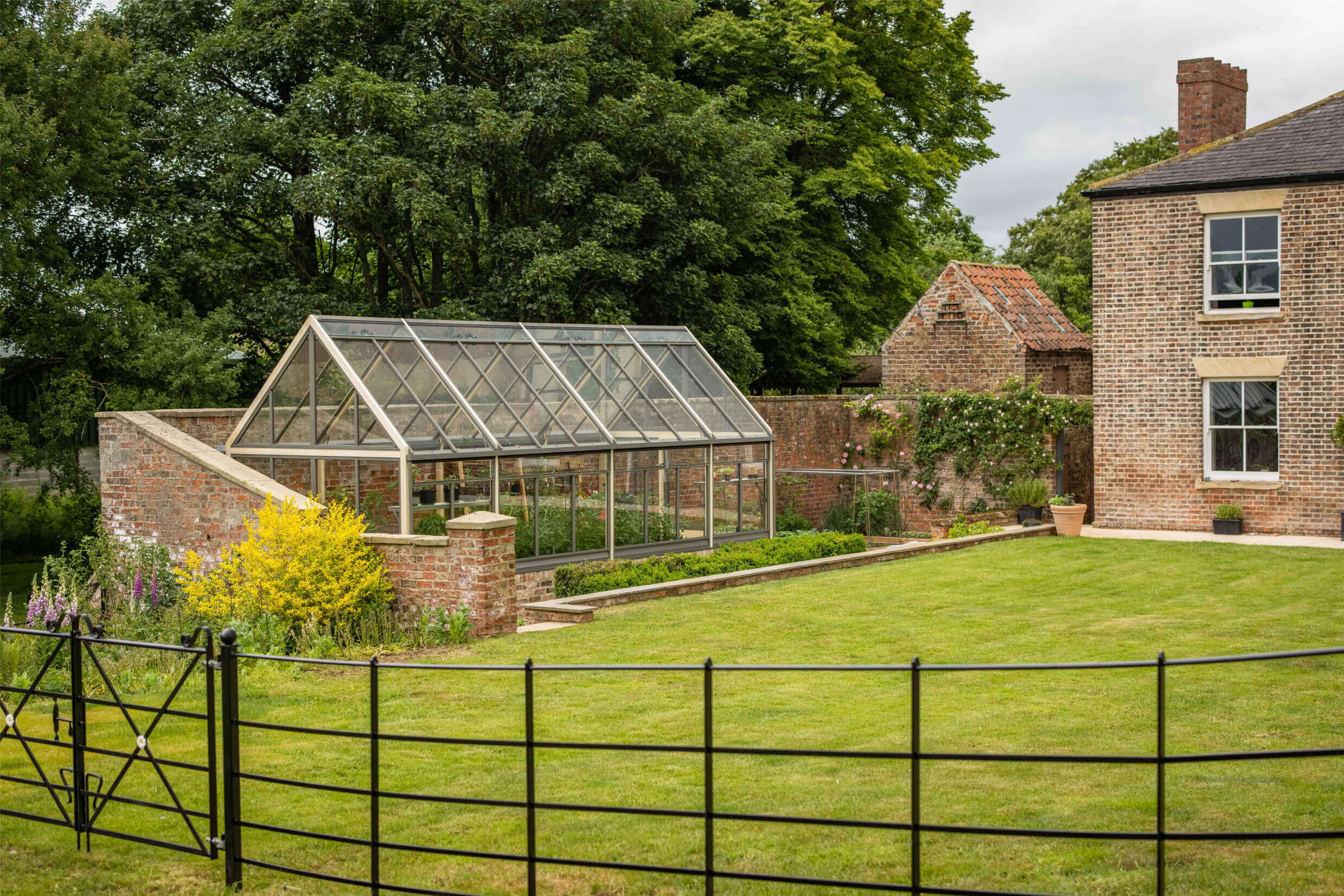 view across garden to large greenhouse against a wall
